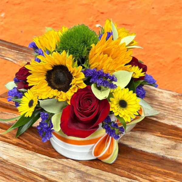 Sunflowers and red roses arranged in a round box with purple accents