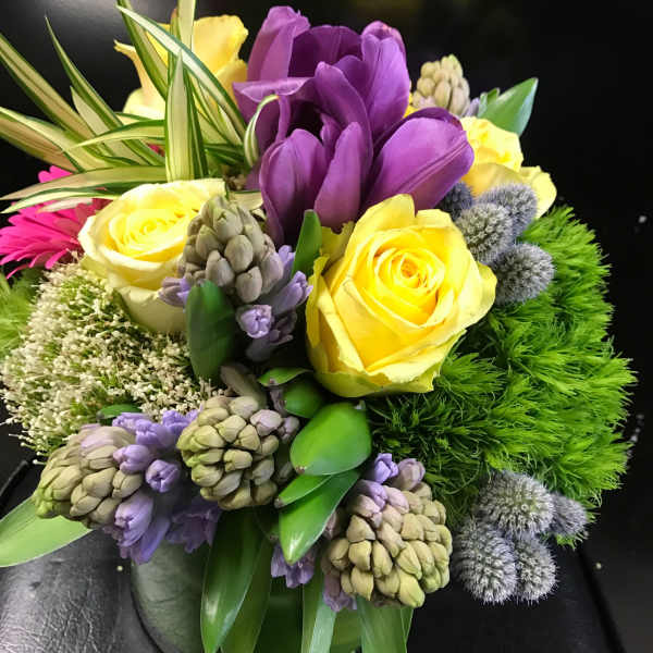 Bouquet of yellow roses and purple flowers in a low vase