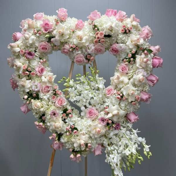 Heart-shaped floral wreath with pink and white roses and orchids on an easel