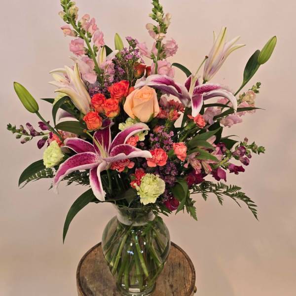 Tall mixed bouquet with pink lilies, roses, carnations, and snapdragons in a clear glass vase