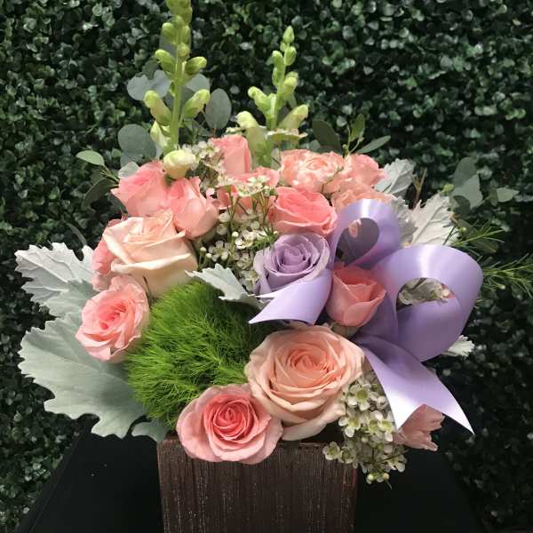 Pink and lavender roses in a square wooden box with a purple ribbon