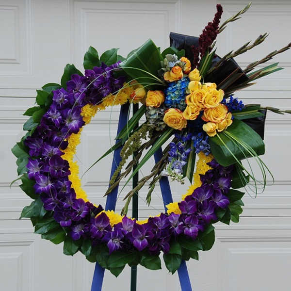 Purple and yellow floral wreath on an easel with roses and orchids