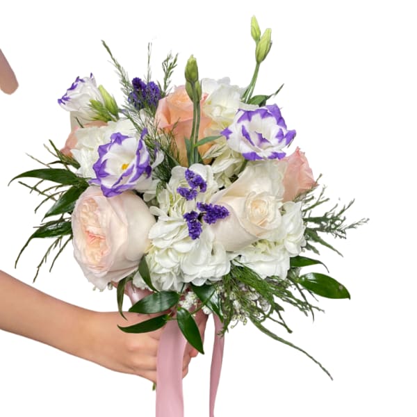 Handheld bouquet of pale roses, white blooms, and purple-edged flowers with a pink ribbon