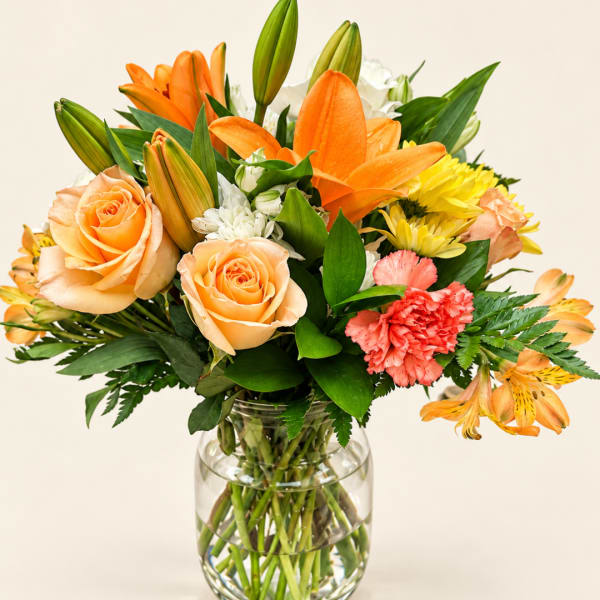 Orange lilies, peach roses, and yellow flowers in a clear glass vase