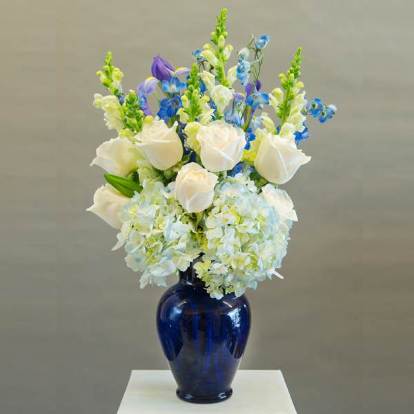 White roses and blue flowers arranged in a cobalt vase