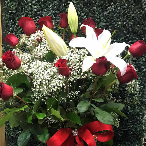 Red roses and white lilies in a clear vase with a red ribbon