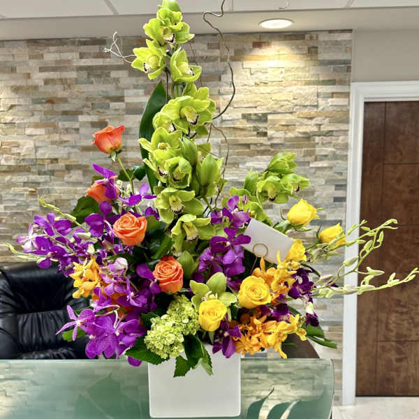 Tall mixed bouquet with green orchids, purple orchids, and roses in a white vase