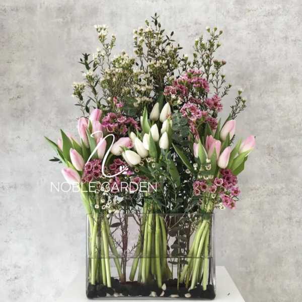 Tall floral arrangement with pink and white tulips in a clear rectangular vase