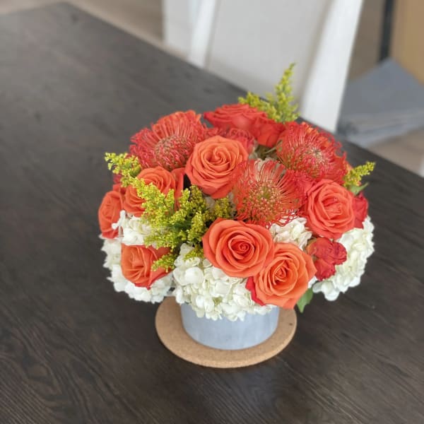 Orange roses and red pincushion blooms in a blue vase