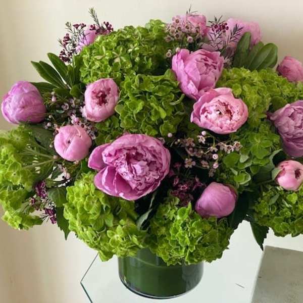 Low round arrangement of bright green hydrangeas and pink peonies in a clear glass cylinder vase.