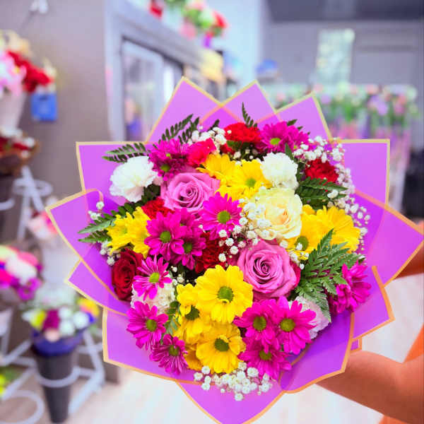 Bouquet of pink, yellow, white, and red flowers wrapped in purple paper