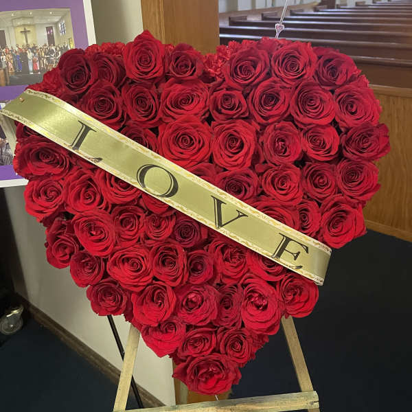 Heart-shaped red rose arrangement on an easel with a gold LOVE sash