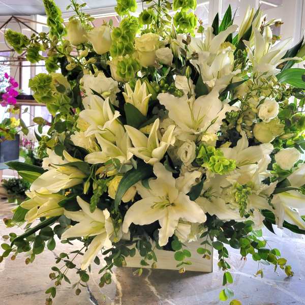 Large white floral arrangement with lilies and green accents in a white container