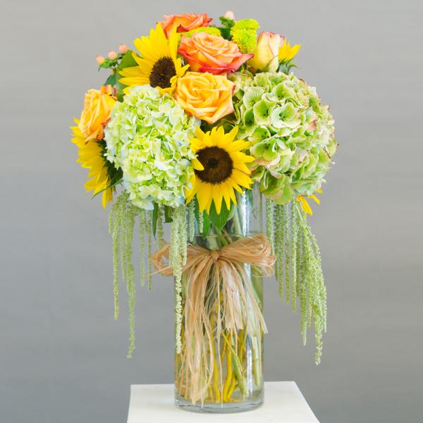 Bouquet of sunflowers, roses, and green hydrangeas in a glass vase
