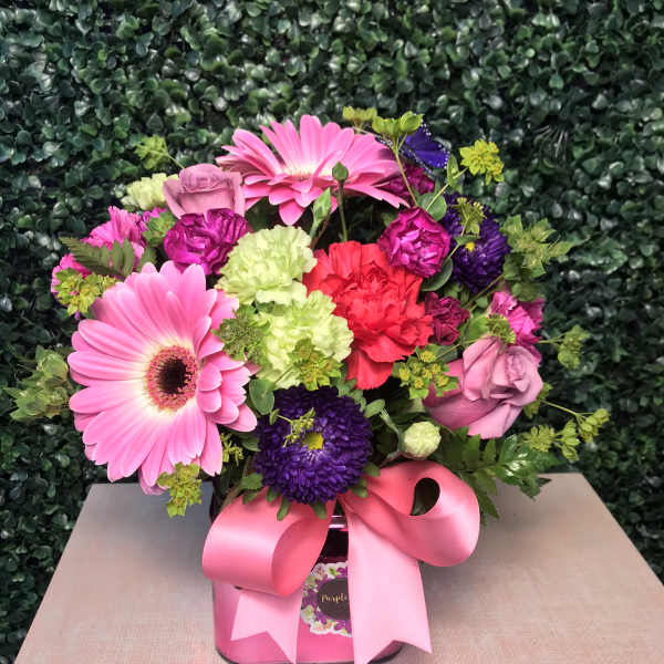 Pink and purple mixed flower arrangement in a pink box with a ribbon