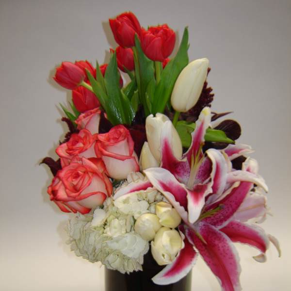 Bouquet of red tulips, pink roses, white lilies, and hydrangea in a dark vase