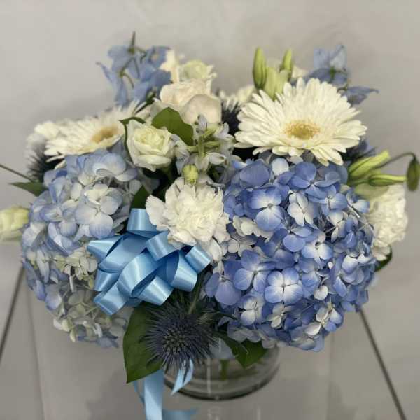 Blue and white bouquet with hydrangeas, gerbera daisies, and a blue ribbon in a glass vase