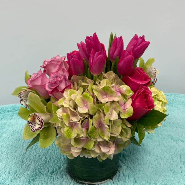 Pink tulips, roses, hydrangea, and orchids arranged in a green vase
