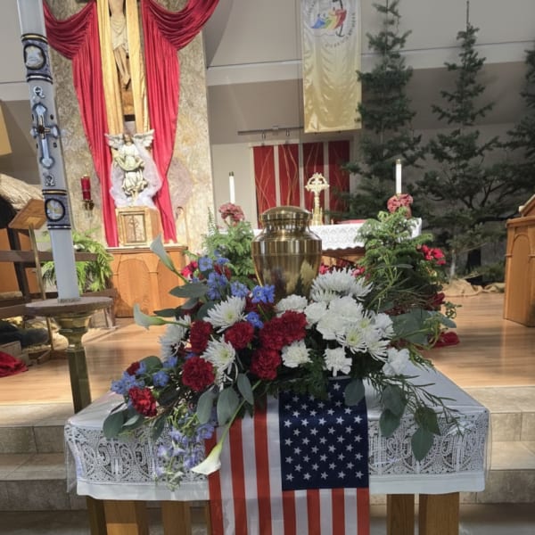 Floral arrangement with red, white, and blue flowers on a table draped with an American flag.
