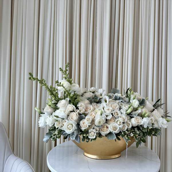 Large white floral arrangement in a gold bowl on a round table