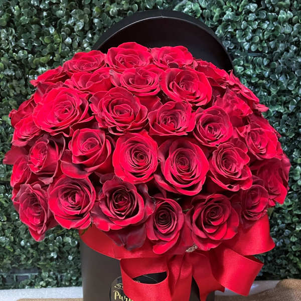 Red roses arranged in a black hat box with a red ribbon