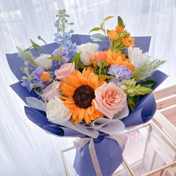 Bouquet of sunflowers, roses, and pastel flowers wrapped in blue paper