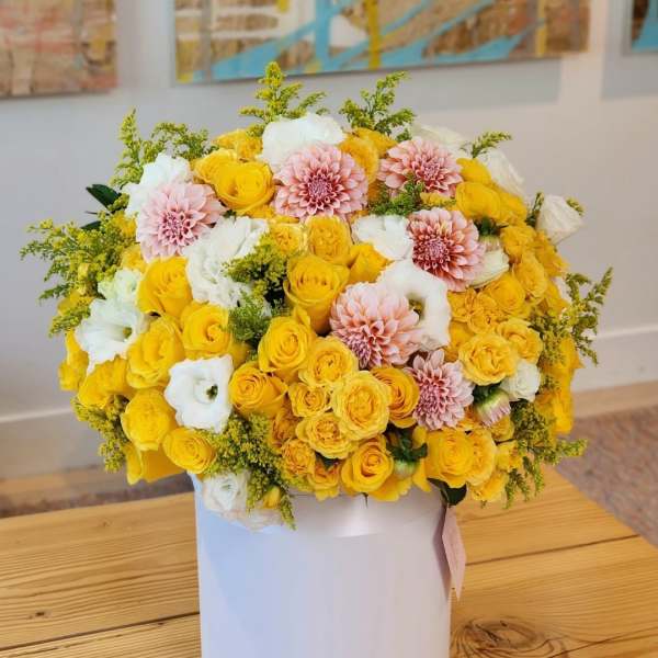 Yellow, white, and blush flowers arranged in a white hat box