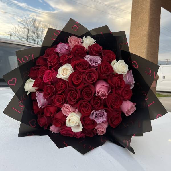 Large bouquet of red, pink, and white roses wrapped in black paper