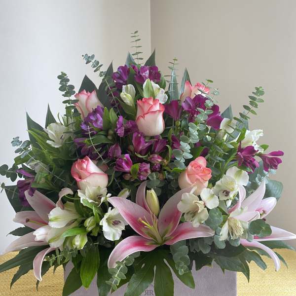 Mixed bouquet of pink lilies, roses, and purple flowers in a box