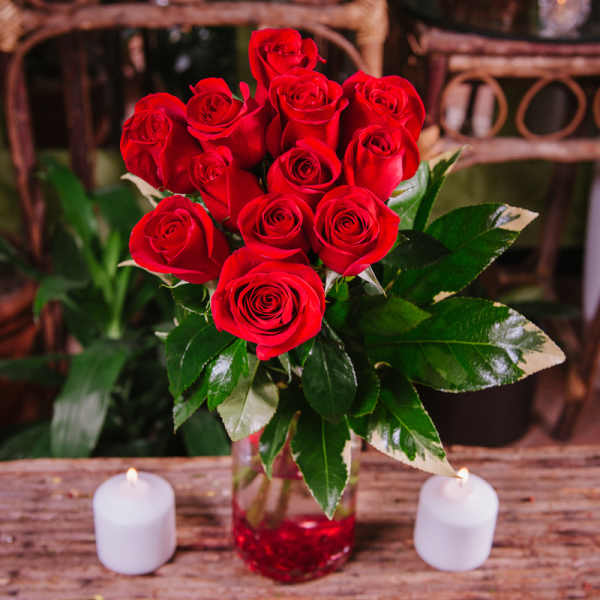 Bouquet of red roses in a glass vase with two white candles