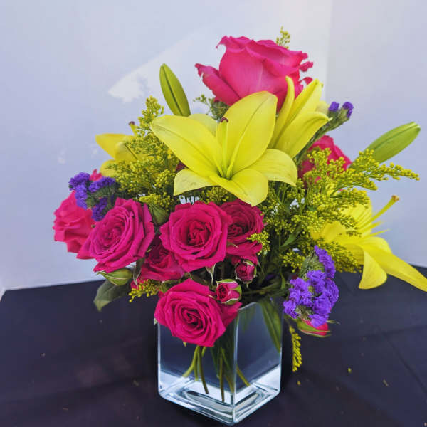 Bright arrangement of hot pink roses and yellow lilies in a clear glass cube vase