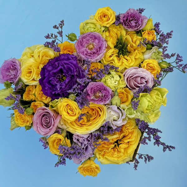 Bright mixed bouquet of yellow, purple, and pink roses on a blue background