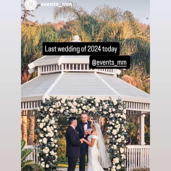 Bride and groom under a white floral wedding arch at an outdoor gazebo