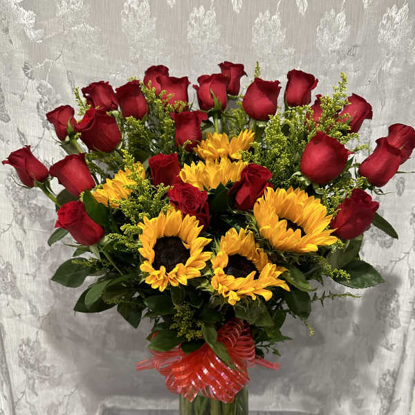 Red roses and yellow sunflowers in a glass vase with a red ribbon