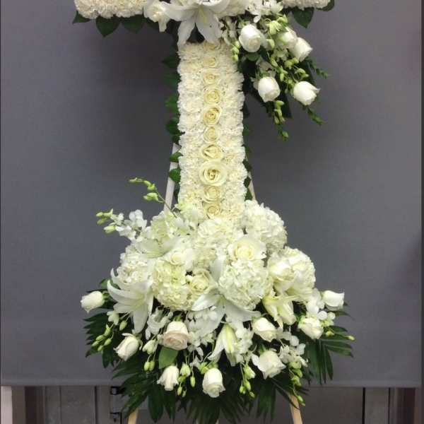 White floral cross on an easel with lilies and roses