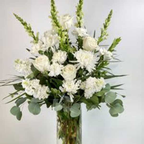 White floral arrangement in a clear glass vase with tall green spikes
