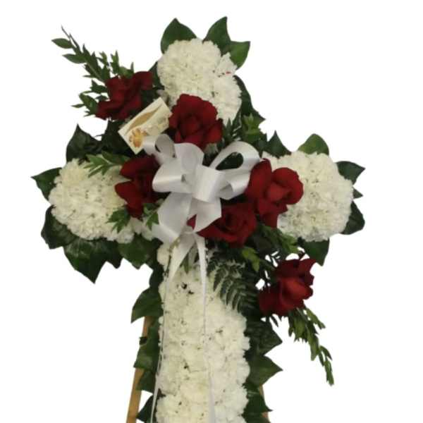 Standing white floral cross with red roses and white bow on an easel