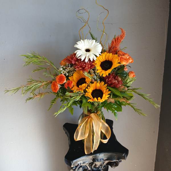 Orange and white flowers arranged in a glass vase with a ribbon
