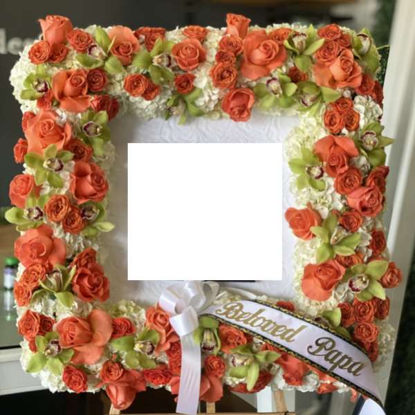 Square floral tribute with orange roses and white flowers on an easel