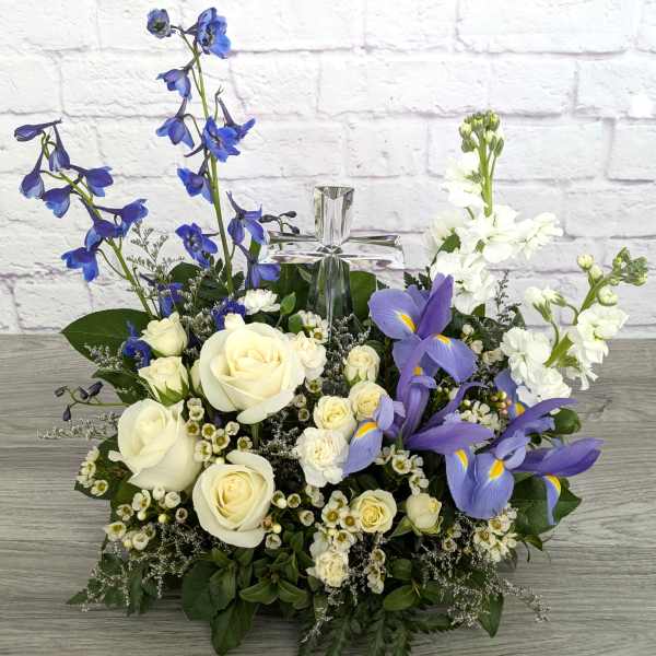 White roses and purple irises arranged around a clear glass cross