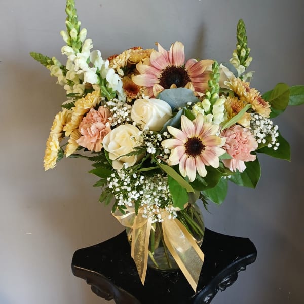 Mixed bouquet in a glass vase with pink sunflowers, cream roses, and peach carnations