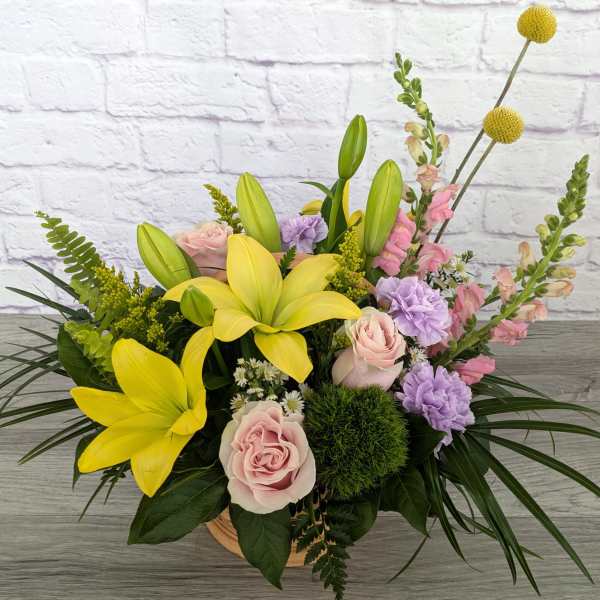 Yellow lilies and pink roses in a low basket arrangement