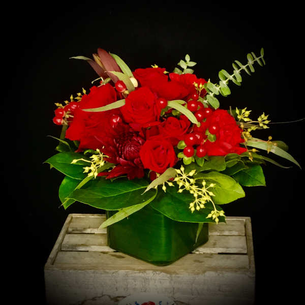 Red rose arrangement in a green vase with berries and greenery
