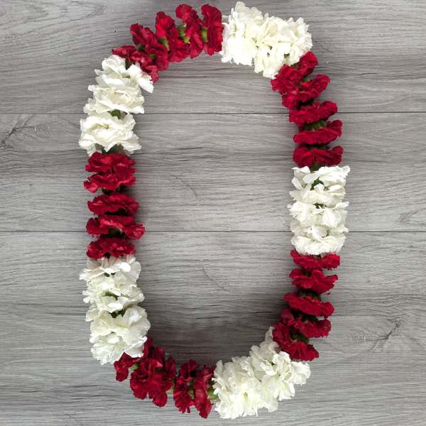 Red and white carnation lei arranged in a loop on a wood surface