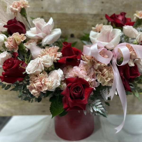 Red roses and pale pink carnations in a burgundy vase with a pink ribbon