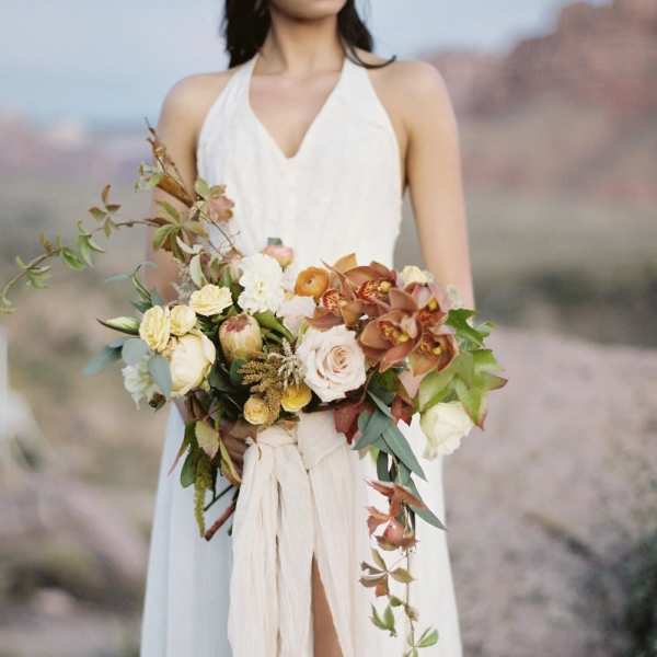 Bride holding a cascading bouquet of cream, peach, and rust flowers