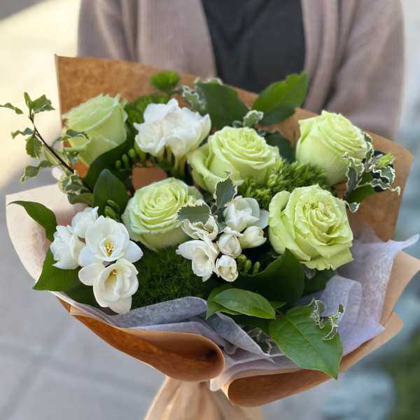 Bouquet of pale green roses and white flowers wrapped in brown paper