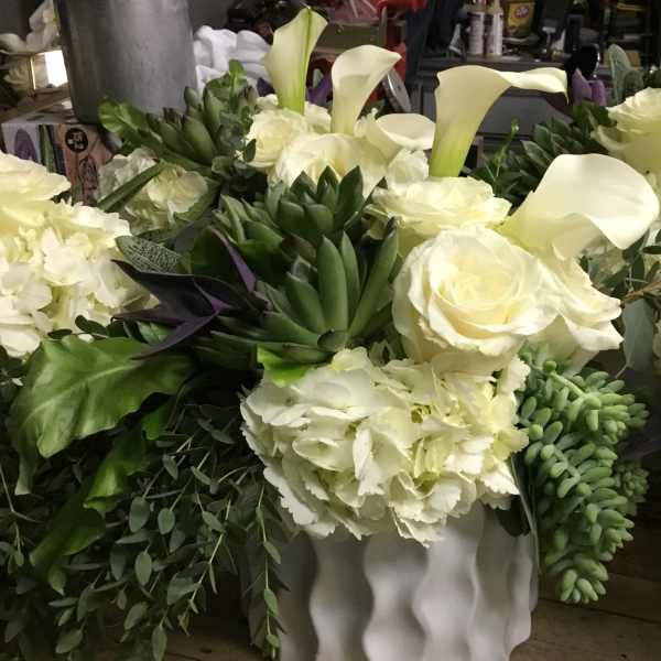White floral arrangement with calla lilies, roses, and hydrangeas in a white vase