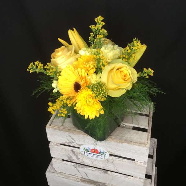 Yellow floral arrangement in a green vase with roses and daisies