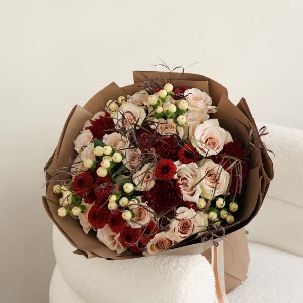 Bouquet of blush roses and red chrysanthemums wrapped in brown paper